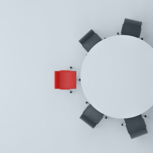 A round board room table with one red chair and six black chairs