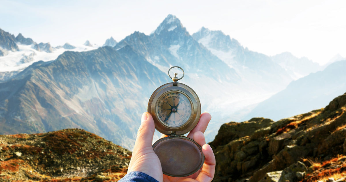 A hiker stands in front of a mountain with a compass in their hand