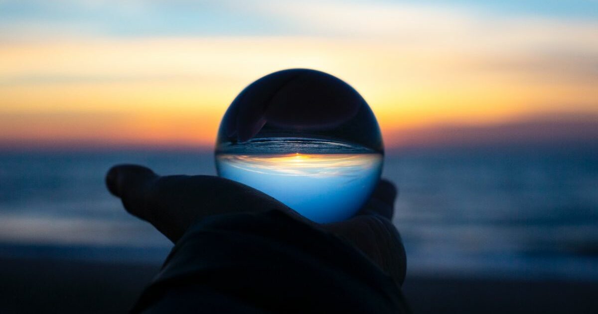 A sunset with the inverse reflection in a glass ball held in the palm of a hand in the centre of the frame
